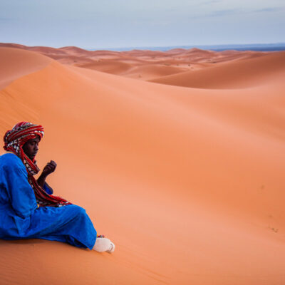 Dopo aver accompagnato tutto il giorno decine di turisti, un giovane cammelliere berbero si concede un attimo di malinconico riposo davanti al tramonto (Merzouga, Marocco, 2010)